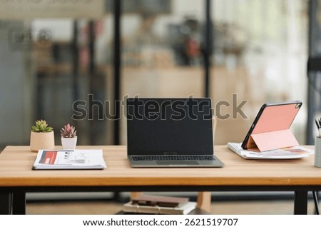 Tablet Laptop Computer, notebook, and eyeglasses sitting on a desk in a large open plan office space after working hours	