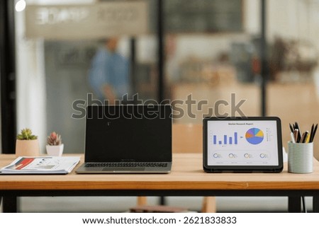 Tablet Laptop Computer, notebook, and eyeglasses sitting on a desk in a large open plan office space after working hours	