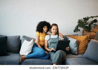 Tablet, love and lesbian couple relaxing on a sofa in the living room networking on social media. Rest, digital technology and young lgbtq women scroll on mobile app or the internet together at home. - Powered by Shutterstock