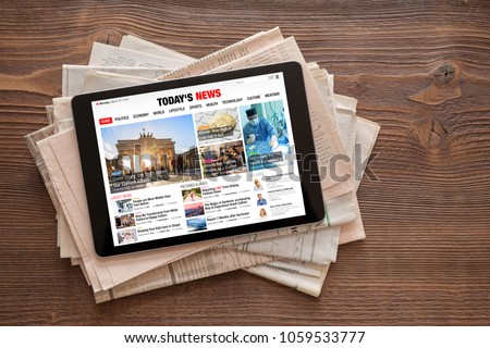 Tablet with news website on stack of newspapers. All contents are made up.