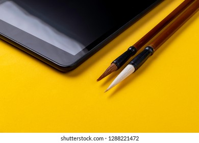 Tablet next to two writing brushes Chinese characters (Mao Pi)  yellow background 