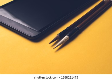 Tablet next to two writing brushes Chinese characters (Mao Pi)  yellow background 