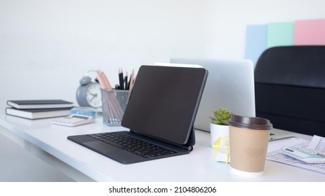 Tablet On White Table. Nearby Is  Paper Graphics, Cup Of Coffee In Meeting Room. Empty Workplace , No People.