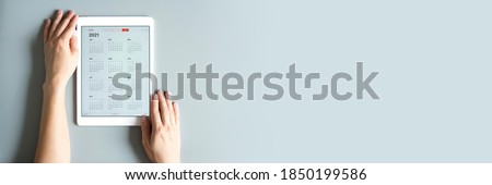 a tablet with an open calendar for 2021 year in a womans hands on a gray background. banner. space for text