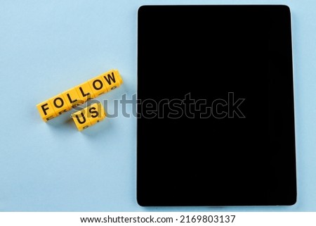 Tablet pc with black screen on blue background. Yellow cube letters with follow us words.