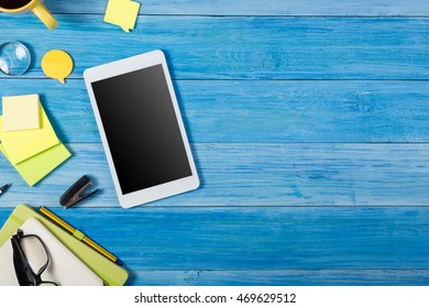 Tablet Pc, Empty Blank Screen On Office Table Desk With Set Of Colorful Supplies, Note Pad, Cup, Pen, Flower Blue Background. Top View And Copy Space For Ad Text