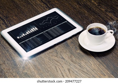 Tablet pc with graphs and cup of coffee on wooden table