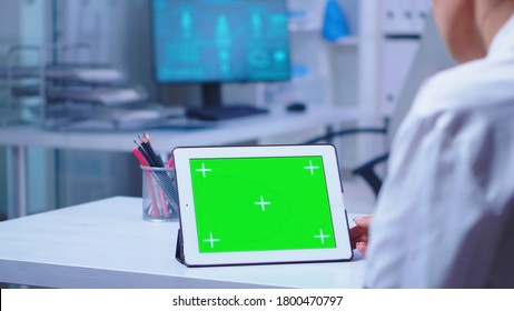Tablet pc with green screen in hospital cabinet used by doctor wearing white coat. Nurse in blue uniform entering in clinic. Doctor in health clinic working on tablet computer with replaceable screen - Powered by Shutterstock