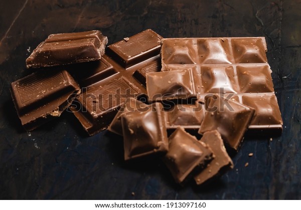 Tablet pieces of dark chocolate on a dark and\
industrial surface.