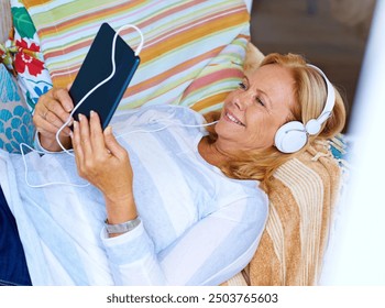 Tablet, relax and senior woman in patio, happy and headphones for movies, thinking and couch of house. Watch, app and old person with subscription of film, smile and grandma with peace in home - Powered by Shutterstock