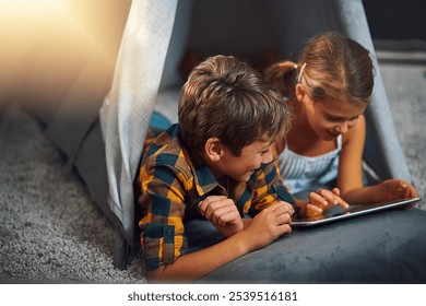 Tablet, rest and kids in tent in home playing online educational game for learning. Relax, digital technology and children siblings watching video for entertainment in blanket fort for fun at house. - Powered by Shutterstock