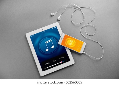 Tablet, smartphone and earphones on gray background. Music player interface on screen.