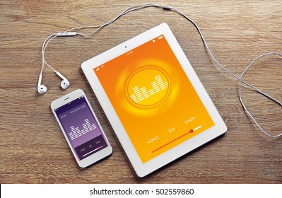 Tablet, smartphone and earphones on wooden background. Music player interface on screen.