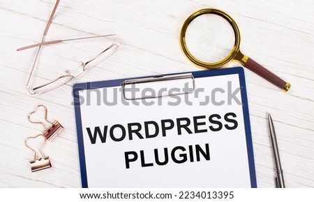 A tablet with the text WORDPRESS PLUGIN on white paper, a magnifier, glasses, golden paper clips and a pen lie on a white office table. Top view, flat lay.
