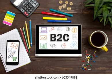 Tablet with web icon B2C on a wooden table with office tools. 