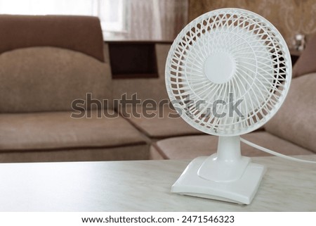 Tabletop white fan with fast rotating blades for cool air flow in home room, electronic fan for cooling on hot sunny day
