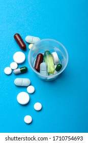 Tablets And Capsules Are Scattered And A Dosage Cup With Tablets. Close-up, Top View, On A Blue Background.