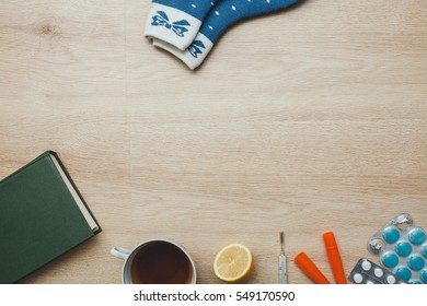 Tablets, thermometer, case, lemon, cup of tea, bandage on wooden background