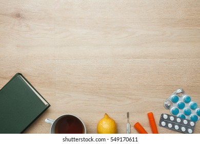 Tablets, thermometer, case, lemon, cup of tea, bandage on wooden background