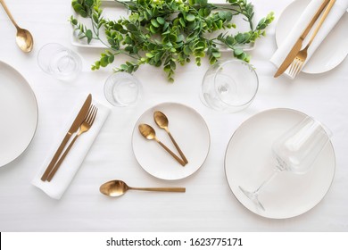 Tableware background in white gold tone.White plates,  gold cutlery,  wine glasses and decorative plant centrepiece - Powered by Shutterstock