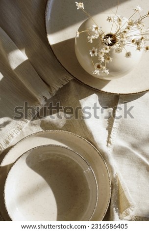 Tableware on a textile napkins, sunlight shadows top view with copy space.Modern kitchen tableware and vase with flowers.Neutral beige color.Business food brand template