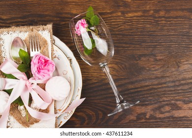 Tableware and silverware with decorations: light pink roses and marshmallows on the wooden background