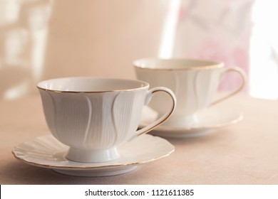 Tableware For Tea Party - Two Cups - On White Tablecloth On Light Pink Floral Background With Sunlight. Close-up, Copy Space