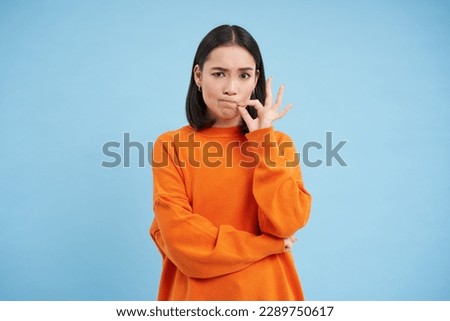 Taboo concept. Asian woman zips her mouth, promises to keep a secret, shuts her lips on lock, stands over blue background.