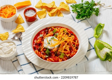 Taco Black Bean Vegetarian Soup With Spiral Fusilli Pasta And Vegetables Topped With Shredded Cheese And Sour Cream In White Bowl On Wood Table, Landscape View