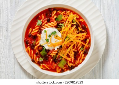 Taco Black Bean Vegetarian Soup With Spiral Fusilli Pasta And Vegetables Topped With Shredded Cheese And Sour Cream In White Bowl On Wood Table, Flat Lay, Close-up