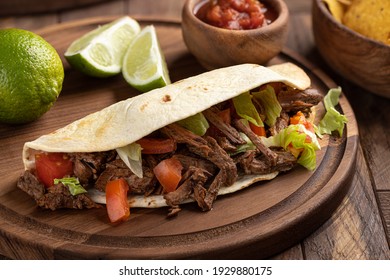 Taco made with roast beef, lettuce and tomato on a tortilla shell on a wooden platter