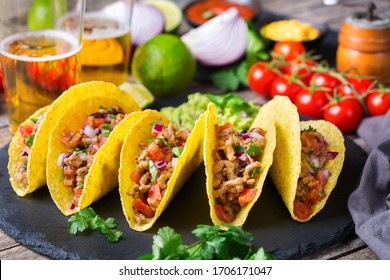 Taco shell ellow corn tortilla chips nachos with ground beef, mince, guacamole, red hot jalapeno chili salsa and cheese sauce with tequila or beer on a table.