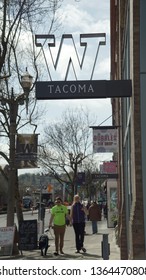 Tacoma WA USA 4/6/2019 University Of Washington Logo Sign Seen From The Sidewalk On Pacific Ave With Pedestrians Walking With Their Dog