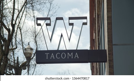 Tacoma WA USA 4/6/2019 University Of Washington Logo Sign Seen From The Sidewalk On Pacific Ave With Pedestrians Walking With Their Dog