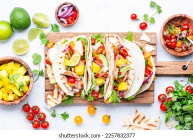 Tacos with grilled chicken, tomato salsa sauce, mango, cilantro and onion in tortilla on cutting board. White table background, top view - Powered by Shutterstock