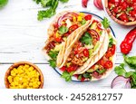 Tacos with ground beef, sweet corn, red beans, tomato salsa sauce and red onion in corn tortillas on plate. Mexican cuisine. Taco party menu. White table background, top view