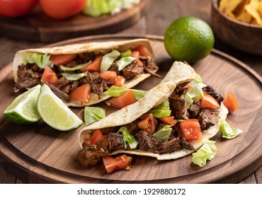 Tacos made with roast beef, lettuce and tomato on a tortilla shell on a wooden platter