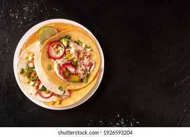 Tacos with pulled chicken, goat cheese and avocado, shot from above on a dark background with copy space