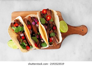 Tacos With Steak, Tomatoes, Onion And Cilantro. Overhead View Serving Board On A White Marble Background.