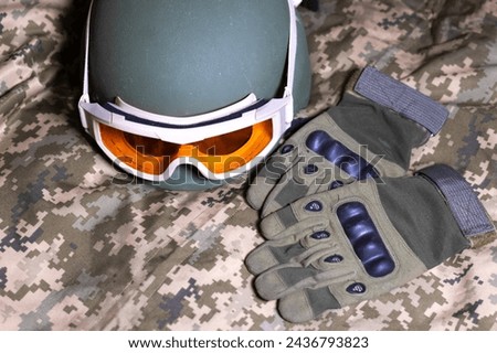 Tactical military gloves, helmet and glasses on the khaki camouflage uniform. Soldier ammunition.