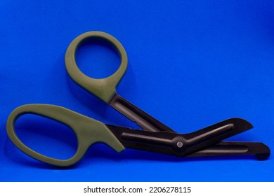 Tactical Scissors Opened On A Blue Background With Dark Green Handles. Military Medicine. High Quality Photo