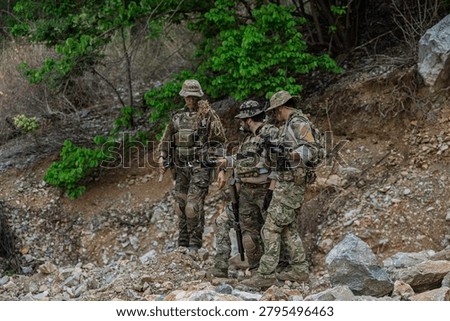 Tactical squad moving cautiously through rugged mountain terrain during field operation. Elite special forces team on patrol in rocky wilderness, demonstrating teamwork and tactical positioning.