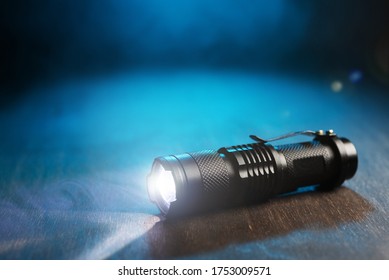 Tactical waterproof flashlight. LED flashlight shines on the table in smoke..