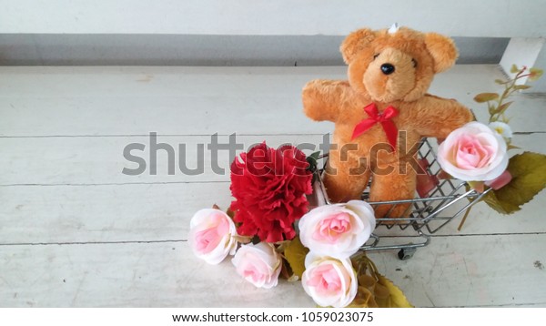 taddy bear\
,pink roses and red carnations flower placed on the cart\
simulationModel cars on a sheet of white\
wood