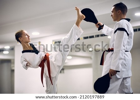 Taekwondo fighter with para-ability practicing high leg kick with her sparing partner at martial arts club.