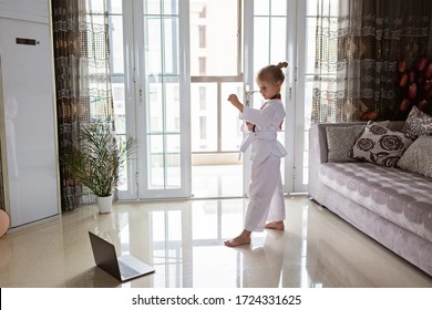 Taekwondo girl in kimono with white belt exercising at home in living room. Online education during coronavirus covid-19 lockdown, self isolation and social distancing concept
