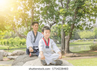 Taekwondo man and kid doing meditation sitting on stone at the park