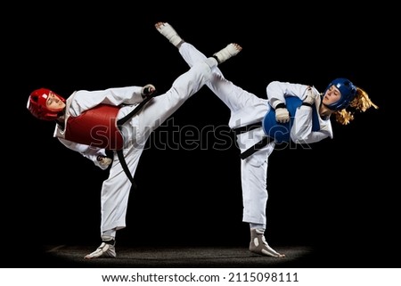 Taekwondo practitioners, two young women wearing doboks training together isolated over dark background. Concept of sport, skills. Concept of sport, education, skills, workout, health