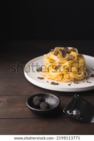 Tagliatelle pasta with black truffle mushrooms. Tagliatelle al tartufo - Italian autumn fresh recipe with black truffle on the wooden table, truffle knife, rustic style, dark key, selective focus  Foto d'archivio © 