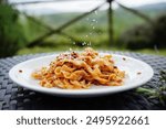 Tagliatelli with bolognaise meat sauce with parmesan. In the background is a hilly green landscape out of focus